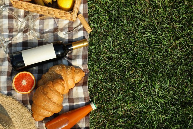 Composition with wine, croissants, fruits and towel on grass, top view