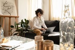 Woman using laptop near draws on papers on sofa in room
