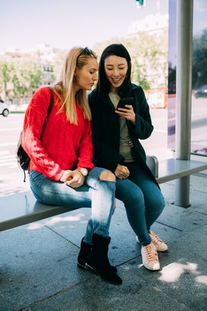 Female friends using smartphone on bus stop
