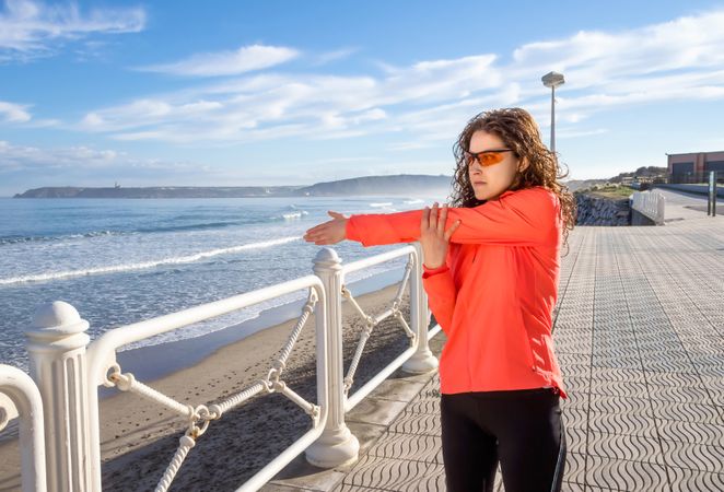 Athletic woman stretching arms before running on the beach promenade on a summer morning
