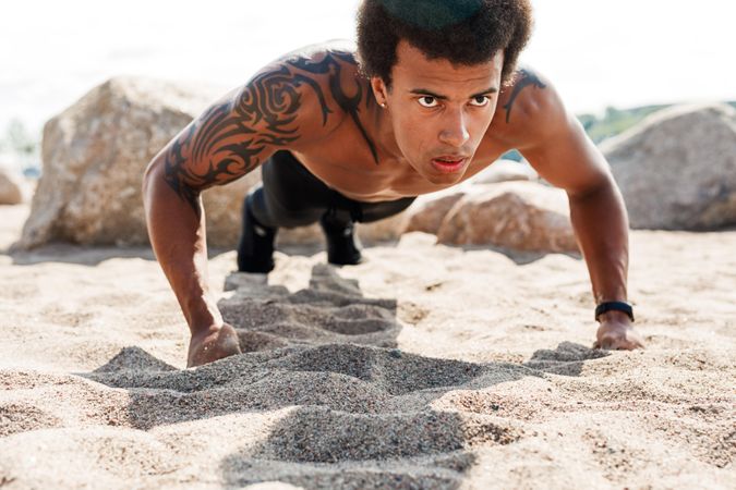 Athletic Black male with tattoo doing pushups in the sand