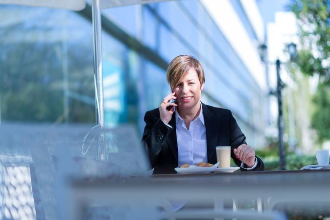 Smiling businesswoman sitting outside with coffee talking on cell phone