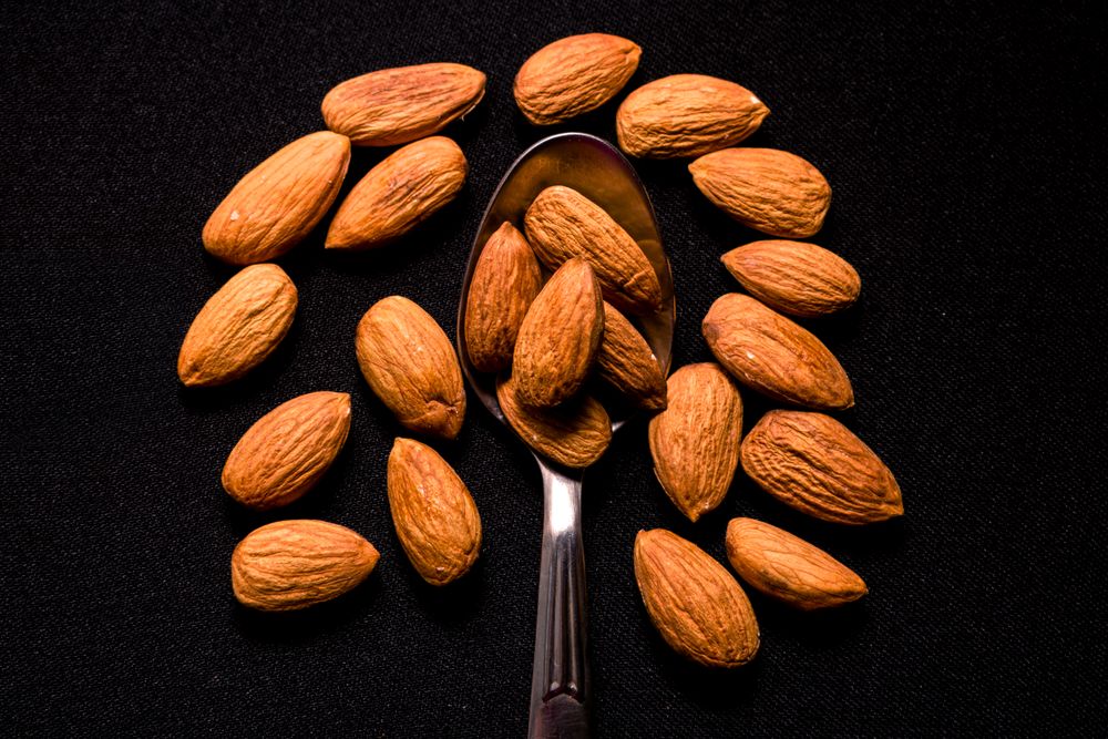 Top view of tasty almonds placed on a steel spoon on a dark background