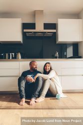 Happy young man and woman sitting on kitchen floor and having coffee 4BvMd4