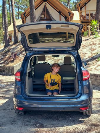 Boy having fun while sitting in trunk near glamping campsite