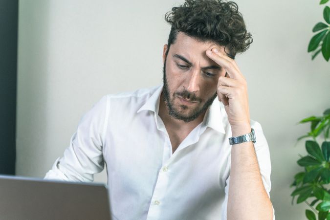 Stressed young man with a headache working on his laptop at a desk.