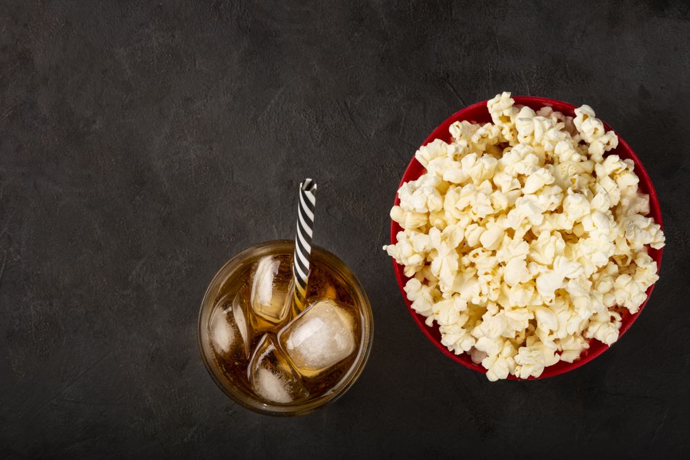 Bowl with salted popcorn and soda on the table.