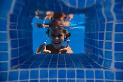 Cheerful boy showing thumbs up in pool