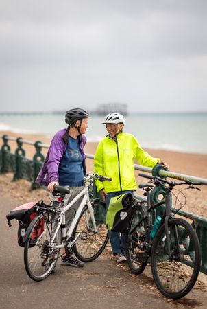Two older people with bikes talking by the seaside
