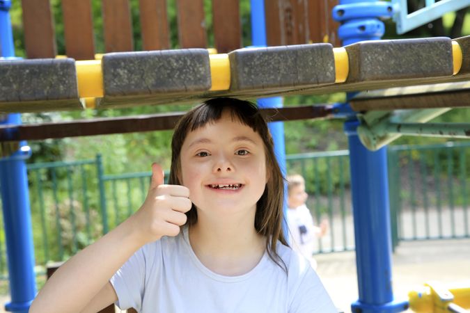 Young child giving a thumbs up outdoors on a playground