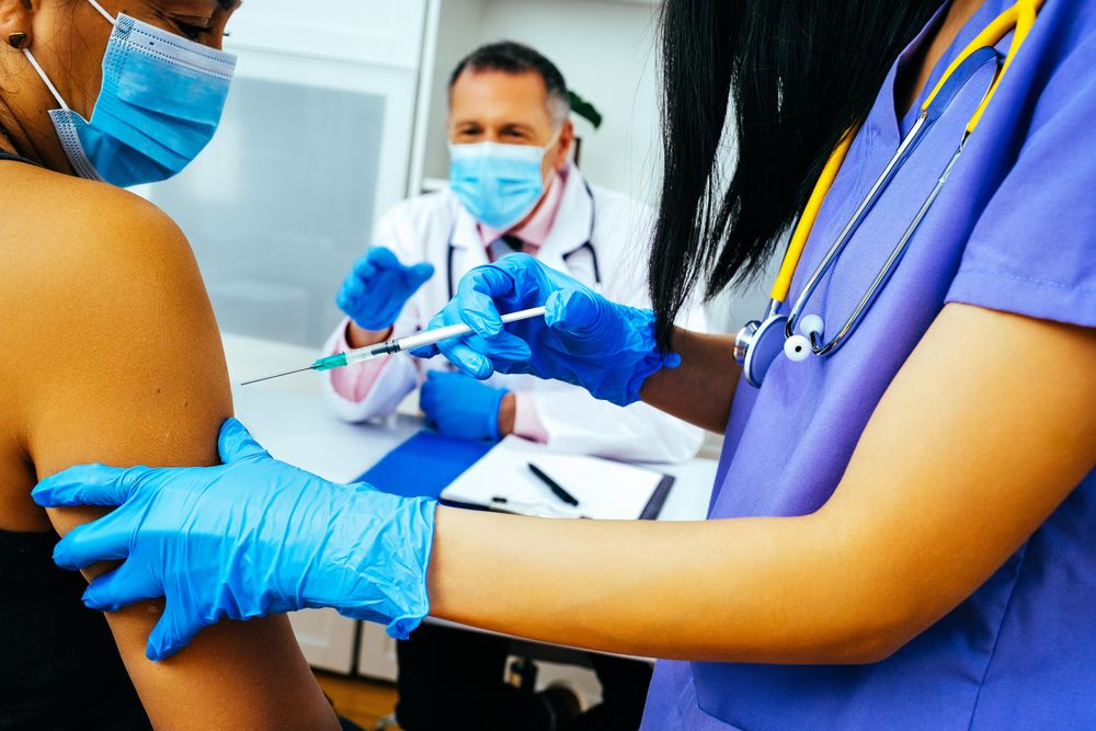 Medical assistant vaccinating female patient in doctor’s clinic