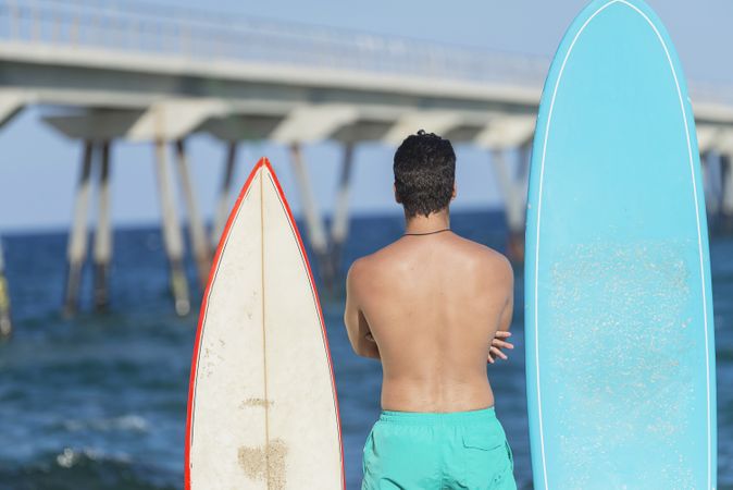 Mid shot of male surfer standing with two boards and looking out to the coast