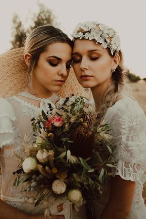 Charming slim brides with flowers in garden with olive trees