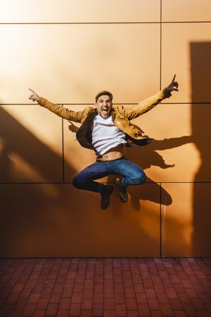Confident guy jumping near modern wall