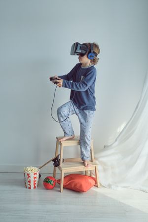 Curious boy in VR glasses and headphones playing with joystick