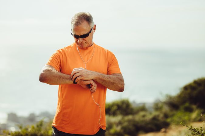 Older man in fitness wear standing outdoors adjusting his wrist watch