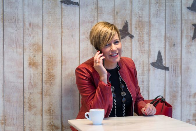 Business woman dressed in red speaking on phone in restaurant with coffee