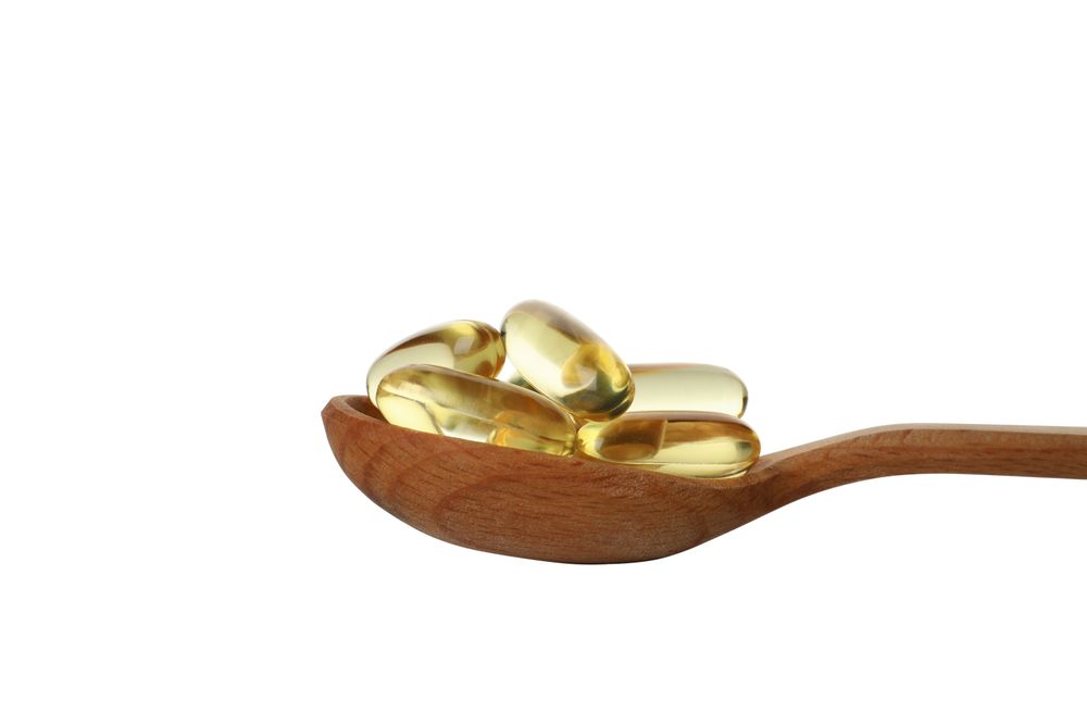 Wooden spoon with omega pills, isolated on blank background