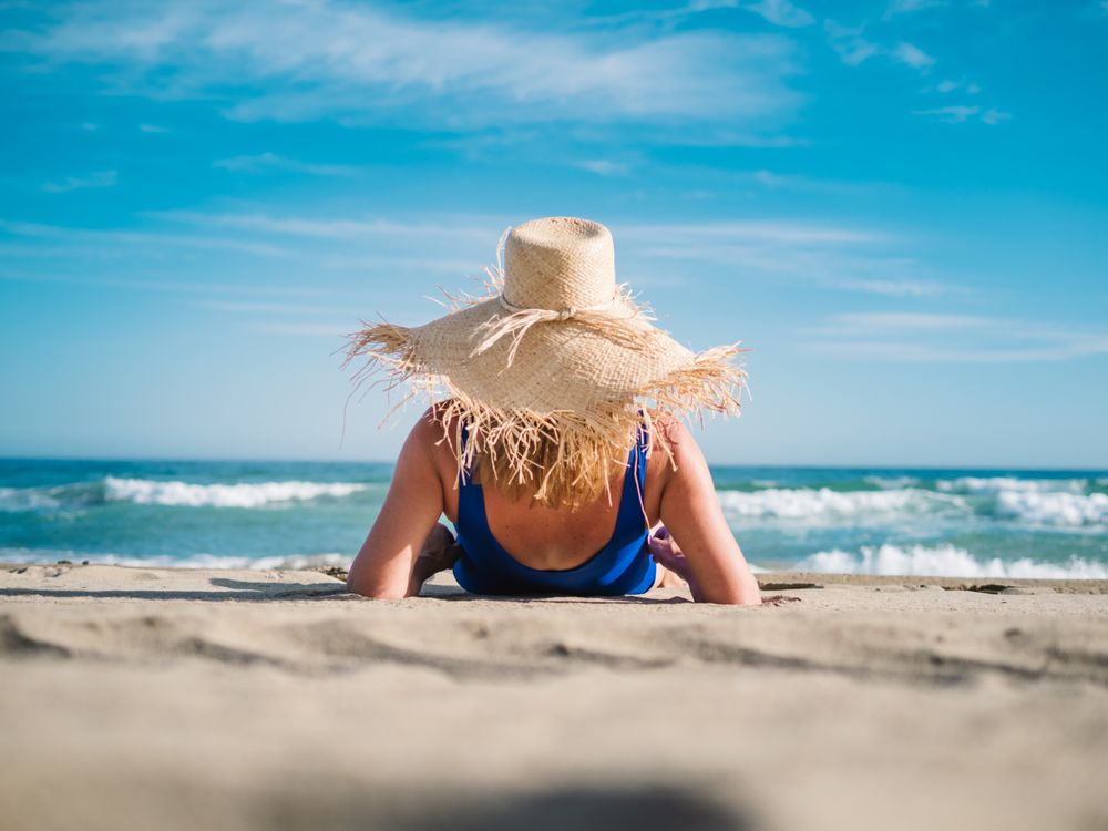 Woman in blue swimsuit and hat on sandy beach