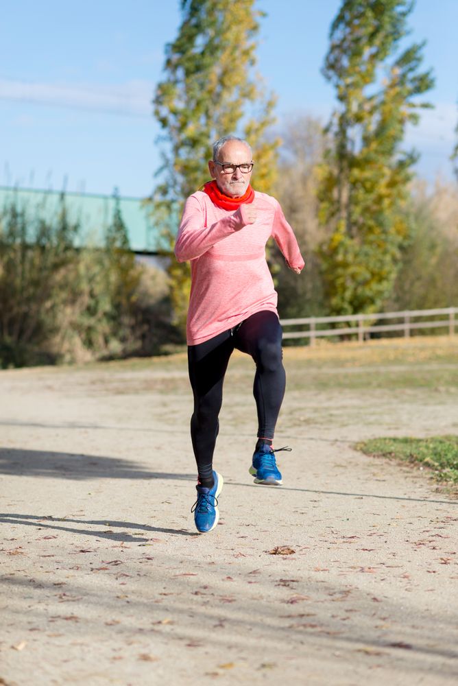 Grey haired man in red shirt and glasses exercising outside doing jumps