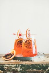 Two glasses of an orange cocktail on board, with blood orange slices, and cocktail picks