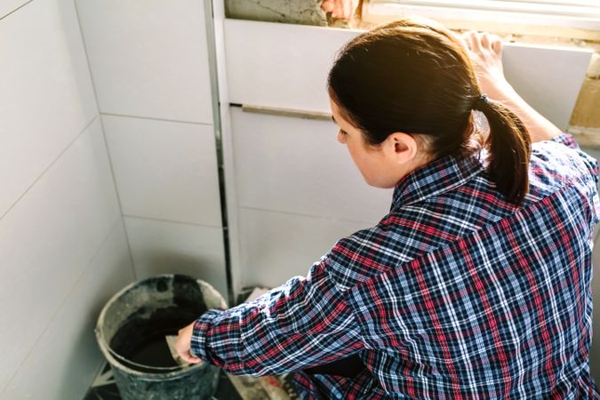 Mason taking cement from bucket to lay bathroom tiles