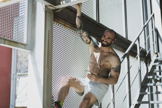 Cheerful sportsman with smartphone hanging near stairway