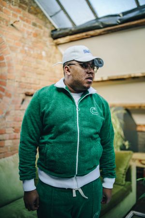 Black man in fuzzy green track suit facing to the side in industrial loft living room