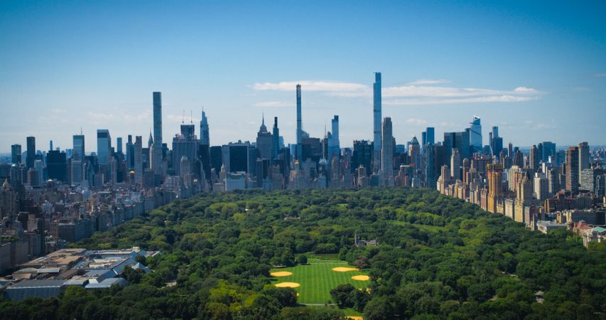 New York City Aerial Landscape Over Central Park with Midtown Manhattan Skyscrapers. Cinematic Drone View of Urban Skyline with Slightly Cloudy Blue Sky