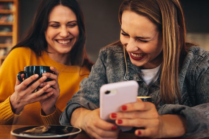 Woman showing something funny on her mobile phone to her friend and laughing