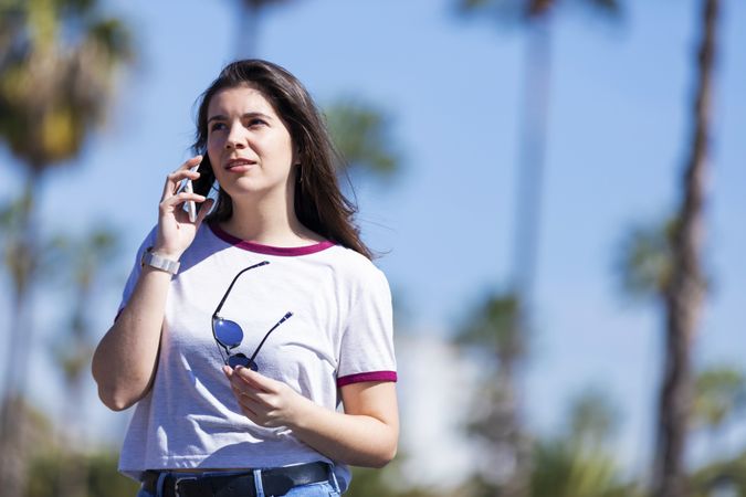 Front view of a beautiful young woman standing outdoors in the street while using a mobile phone on a bright day