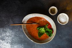 Top view of modern ceramic bowl of gazpacho soup with basil leaves and seasoning