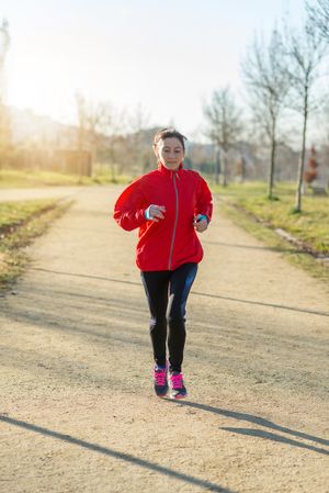 Woman in red jogging outdoors in park on sunny fall day