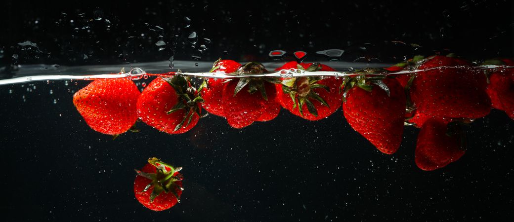 Side view banner of water on dark background with floating strawberries