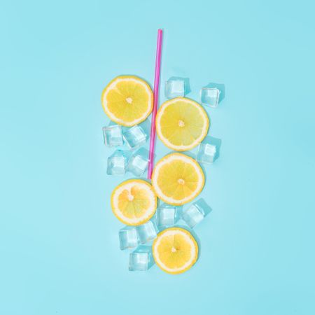 Creative summer background composition with lemon slices, straw and ice cubes