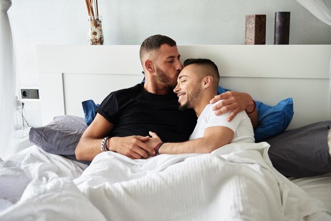 Smiling gay couple hugging and kissing on bed