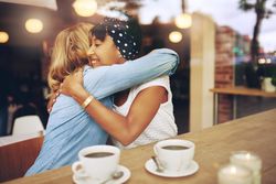 Two female friends hugging in a cafe window