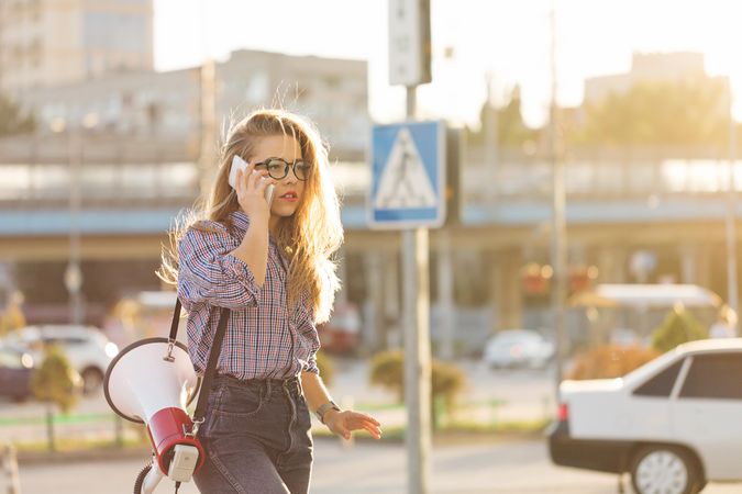 Woman walking outside speaking on phone with megaphone dressed in checkered shirt