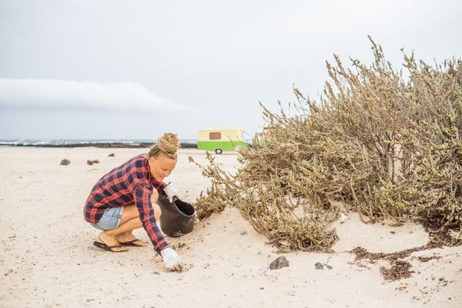 Content modern woman picking litter from sandy seashore