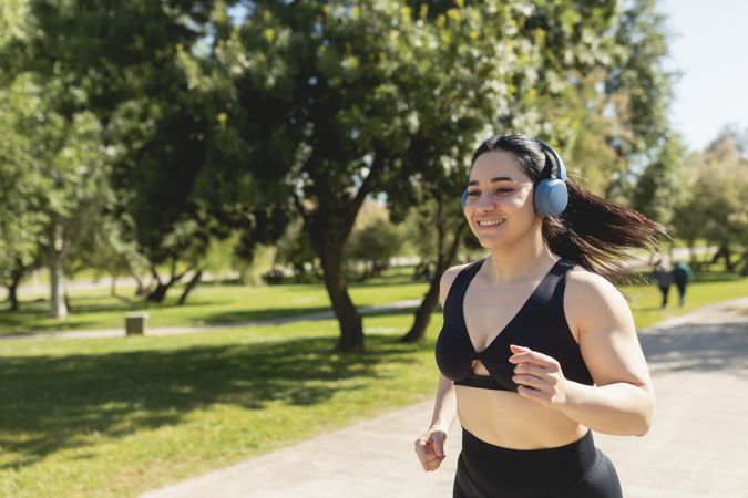 A young woman running around the park, happy, while listening to music with headphones, Zaragoza, Spain