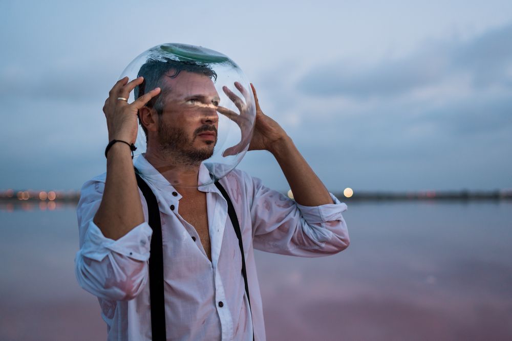 Man with fish tank on head standing at seashore