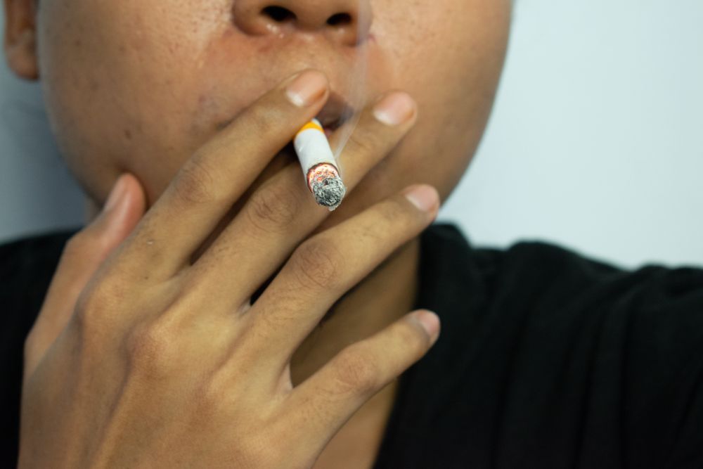 Unrecognizable man holding a lit cigarette to their mouth