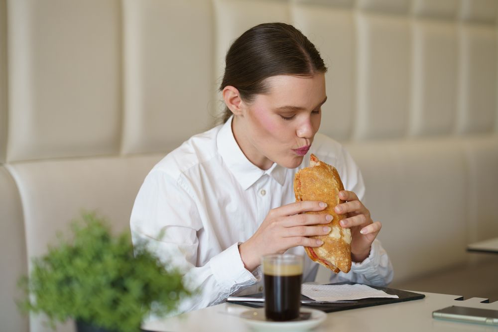 Starved businesswoman eating sandwich and drinking coffee in a cafeteria