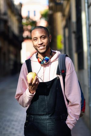 Vertical shot of happy male on European street eating an apple
