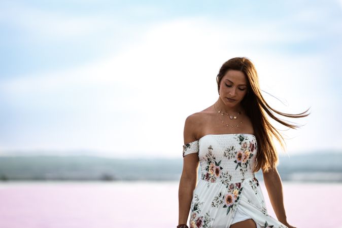 Peaceful woman in white dress walking ankle deep in pink lake