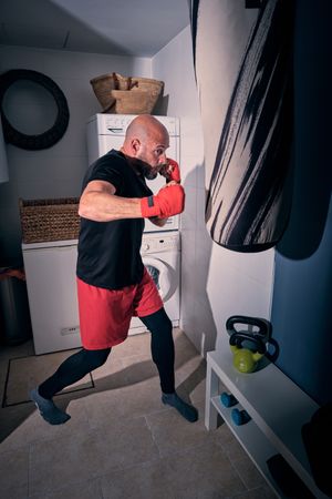 Man training boxing in the laundry room at home with a bag