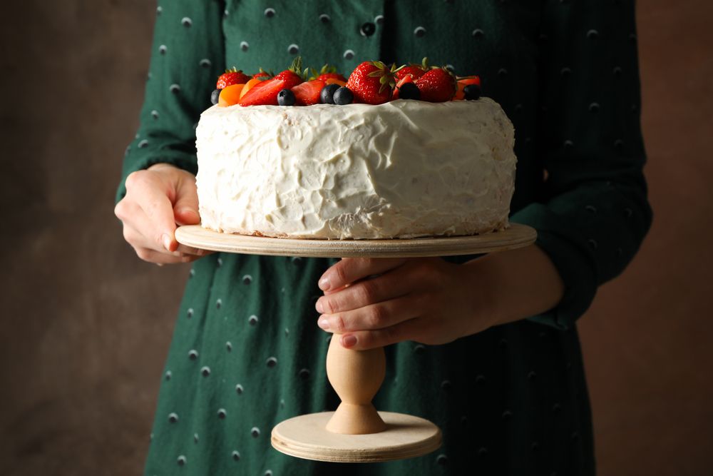 Woman holds berry cream cake against brown background. Delicious dessert