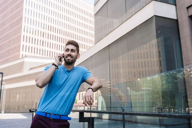Smiling man leaning on glass railing outside talking on mobile phone