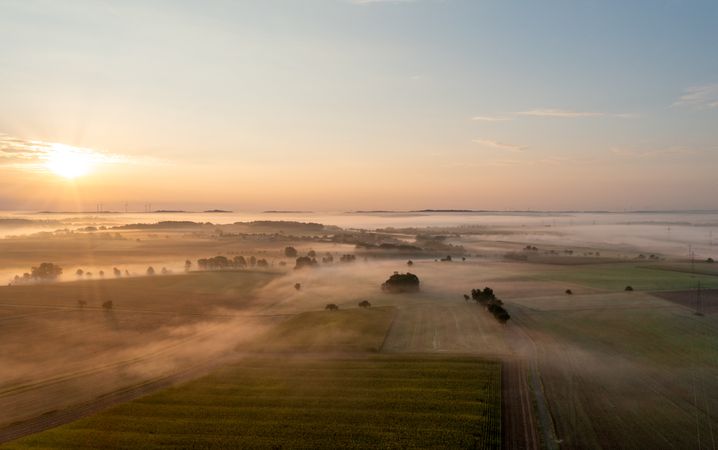 Aerial drone view of rolling landscapes at golden hour with agricultural fields enlightened by sunrise