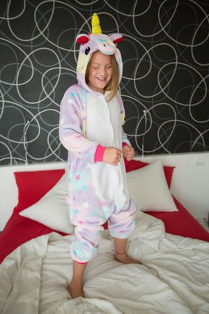 Cheerful girl in unicorn pajama having fun on bed